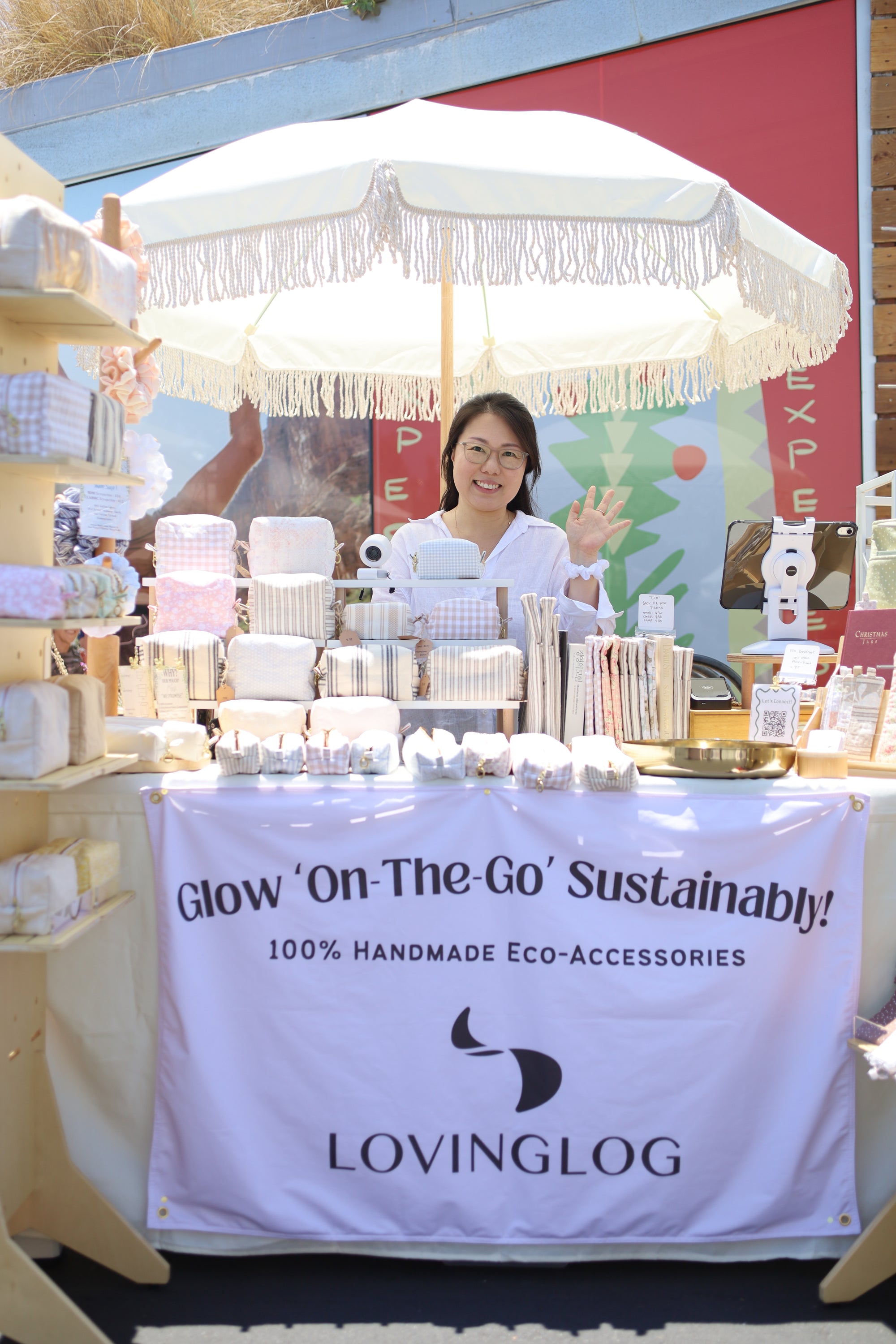 Woman behind a table with handmade eco-accessories at an craft marker, featuring the brand 'LOVINGLOG'.