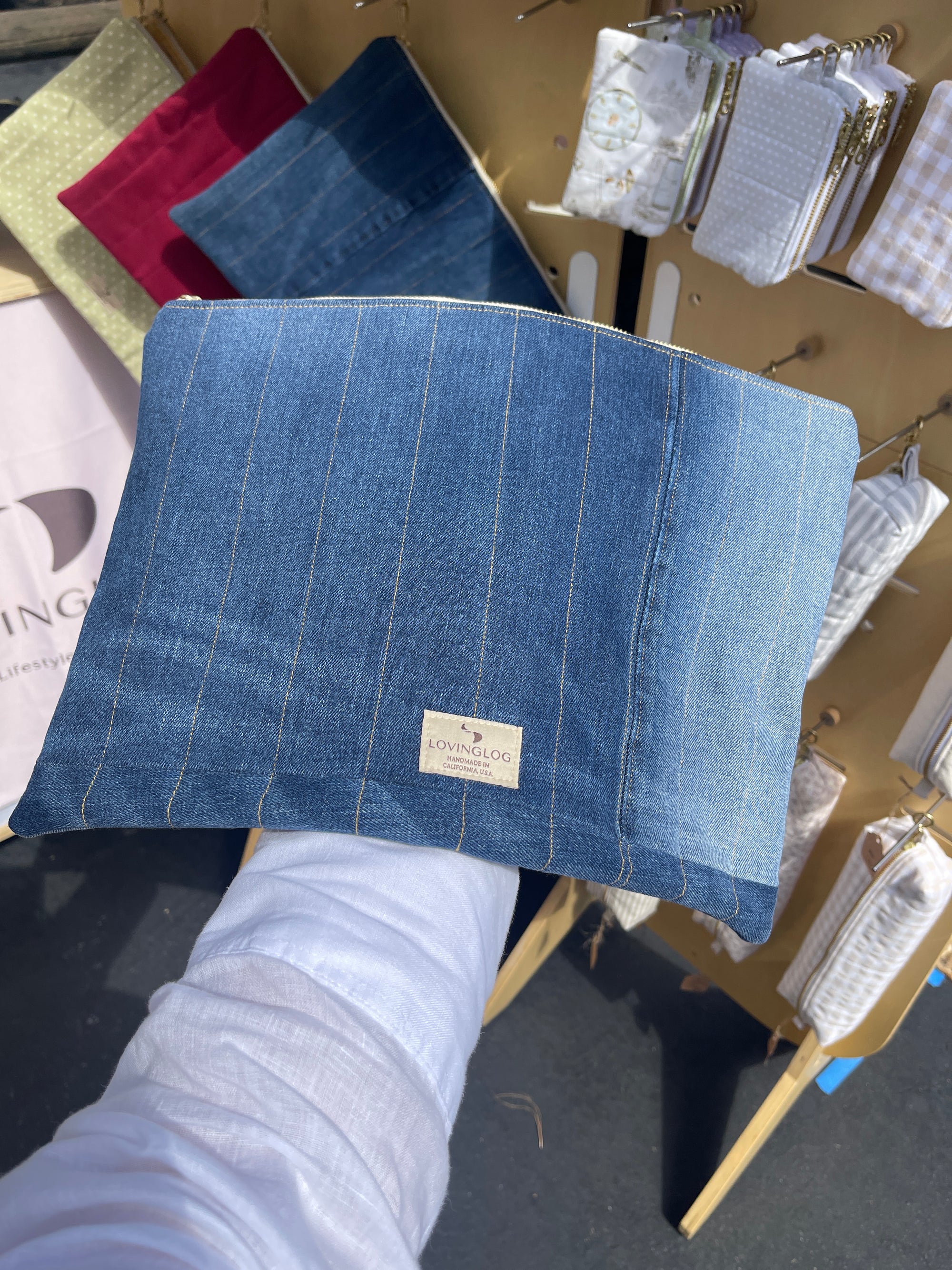 Handmade eco blue denim laptop sleeve held by a person other fabrics in the background