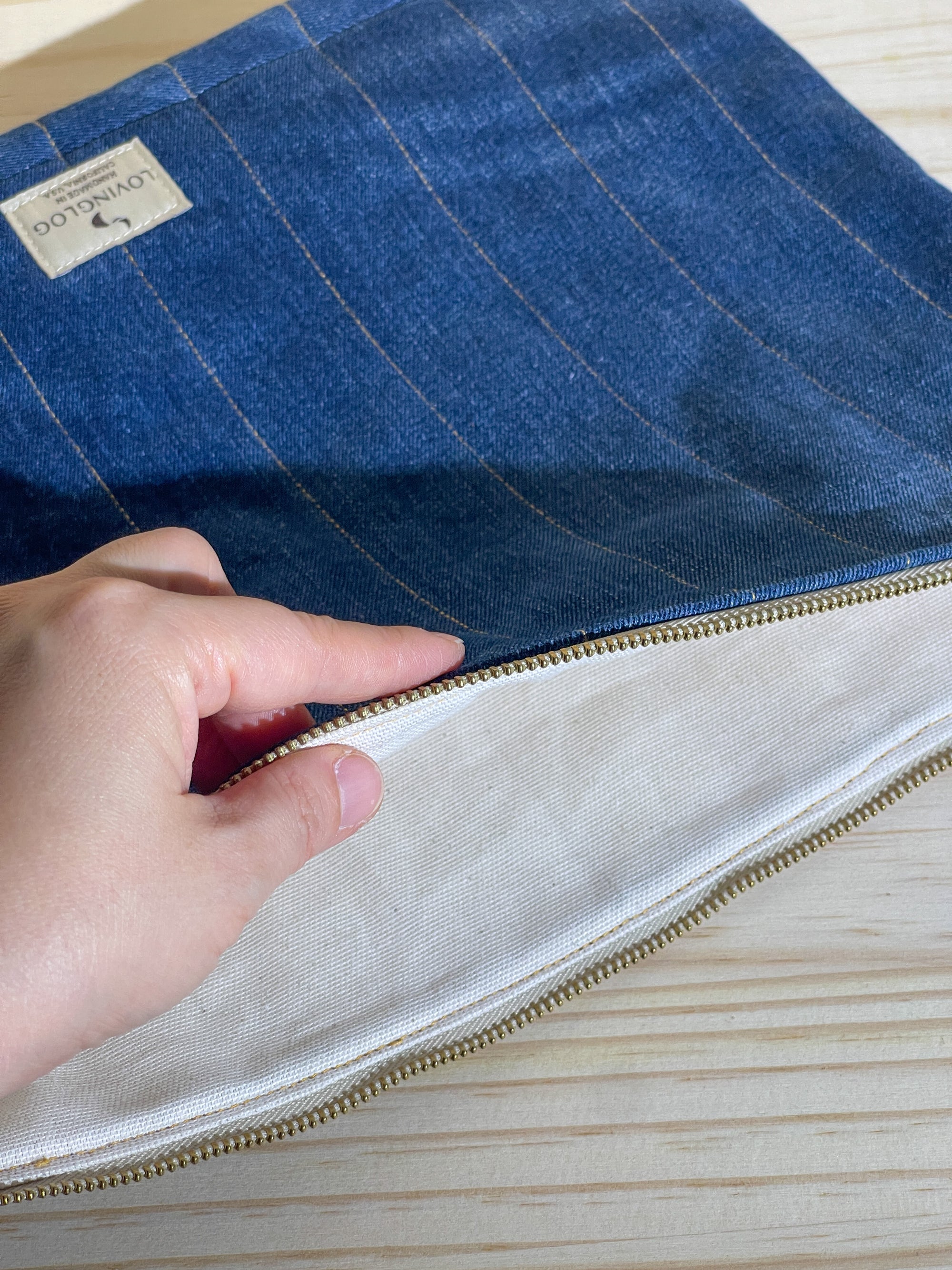 Hand opening a handmade eco blue denim sleeve with a beige interior on a wooden surface.