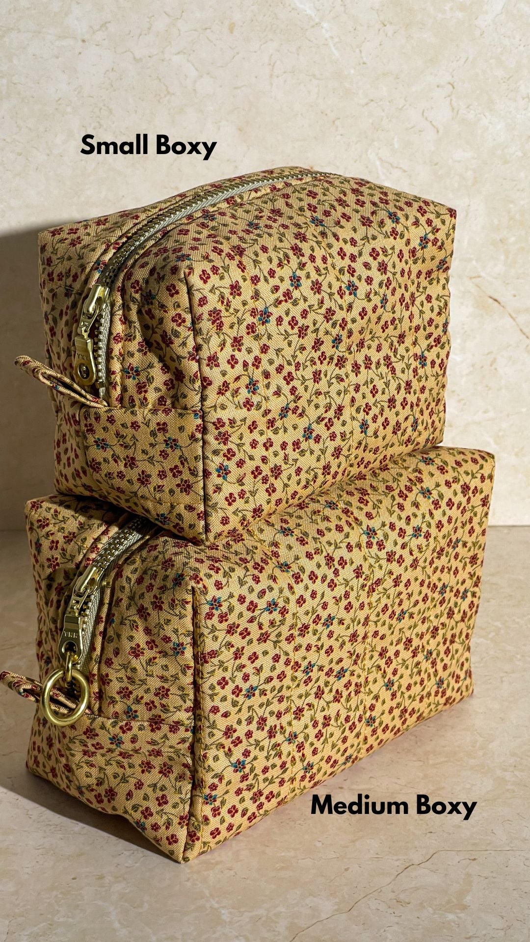Two handmade sustainable quilted cotton floral-patterned boxy pouches, makeup bags, one small and one medium, on a beige surface.