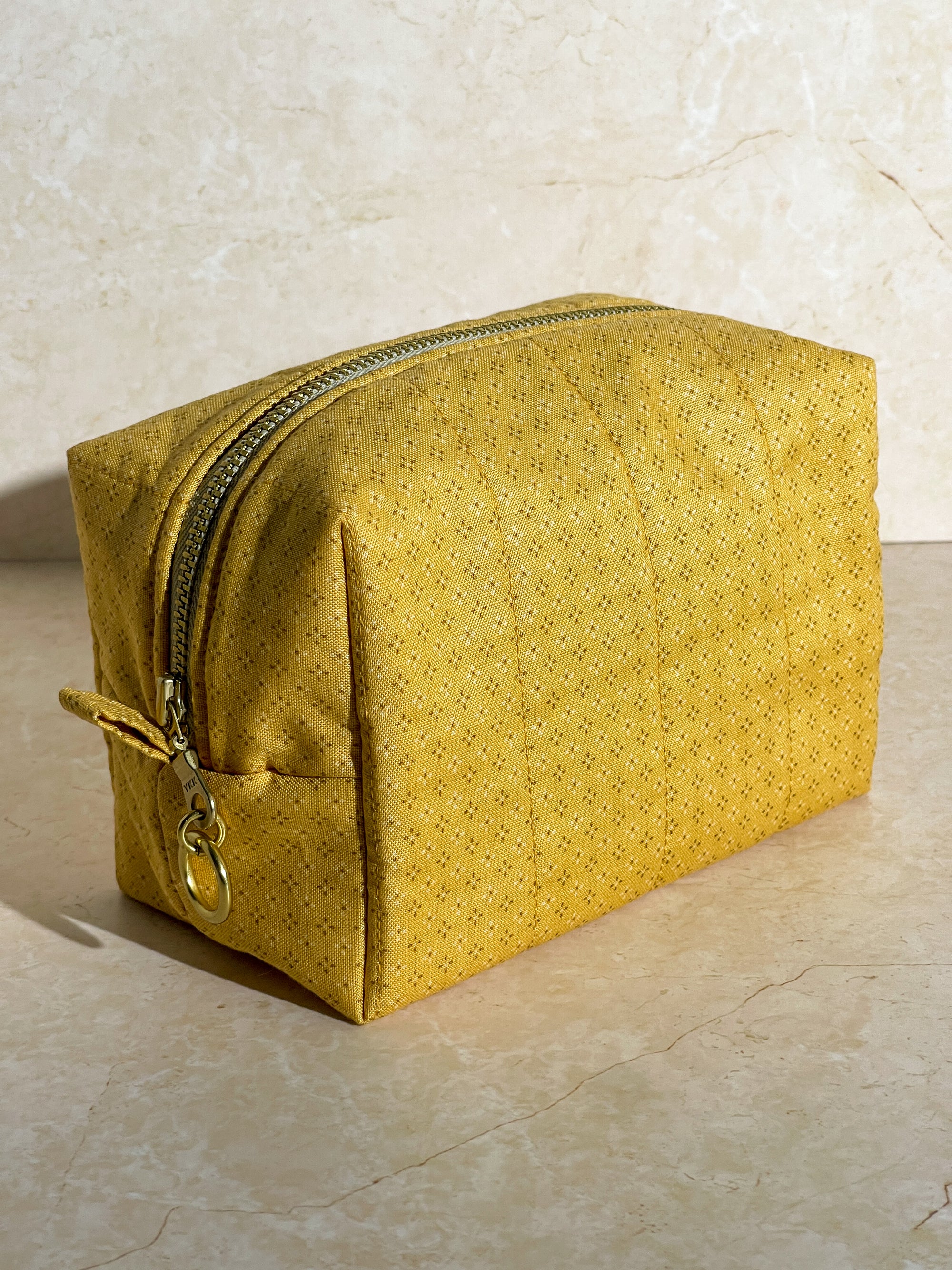 Dimensional view of the handmade sustainable quilted mustard yellow cotton boxy pouch, highlighting the gold zipper detail.