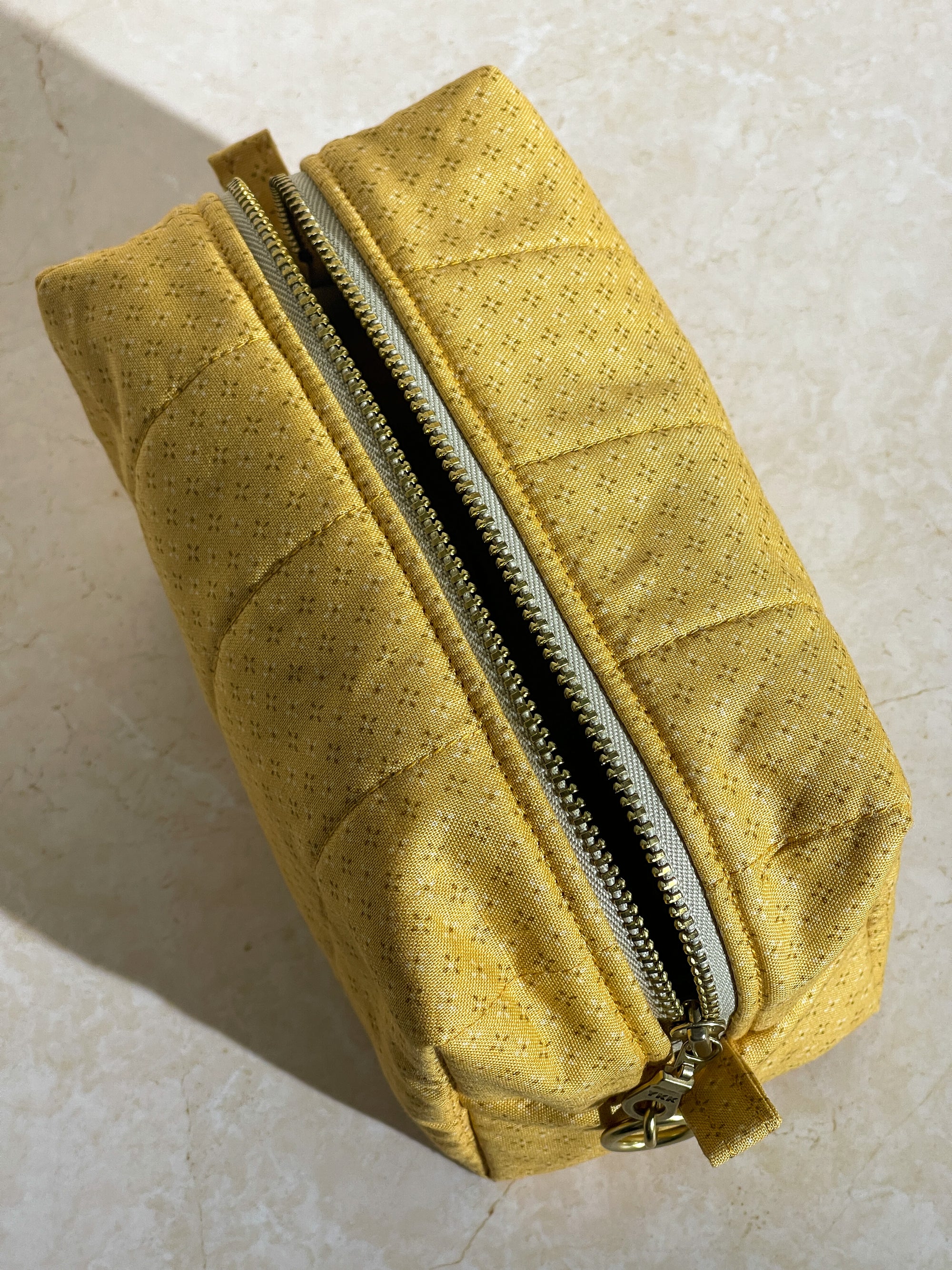 Top view of the handmade sustainable quilted mustard yellow cotton boxy pouch, highlighting the gold zipper detail.