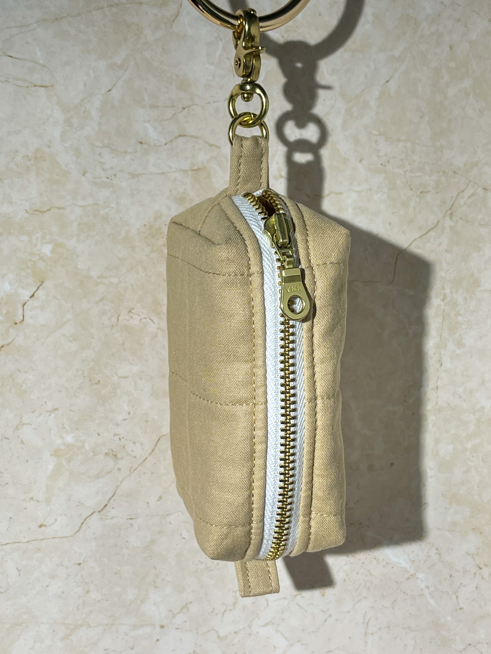 Handmade khaki fabric pouch with gold zipper and keychain on a beige marble background