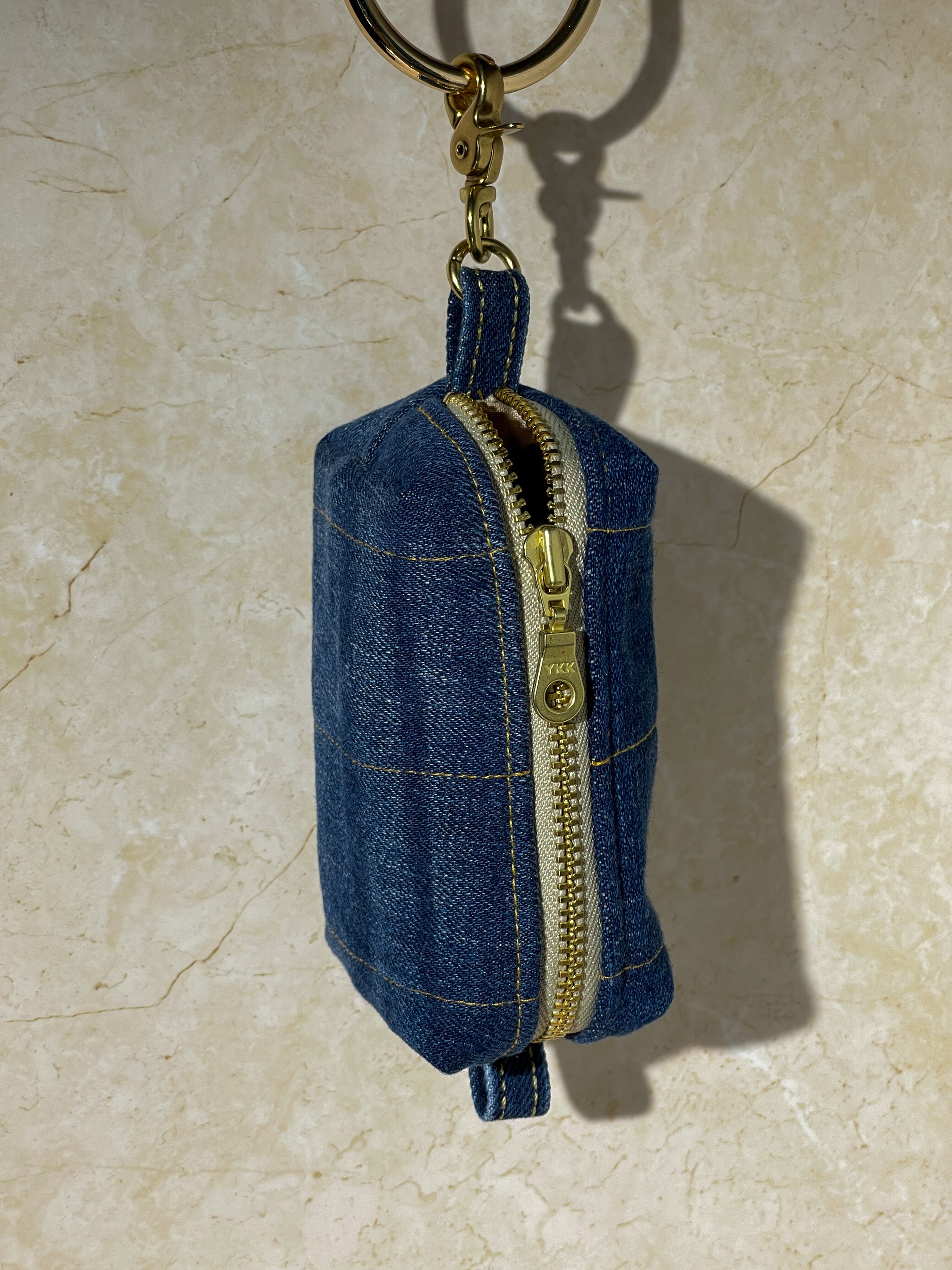Blue upcycled denim keychain pouch with gold zipper on a beige surface