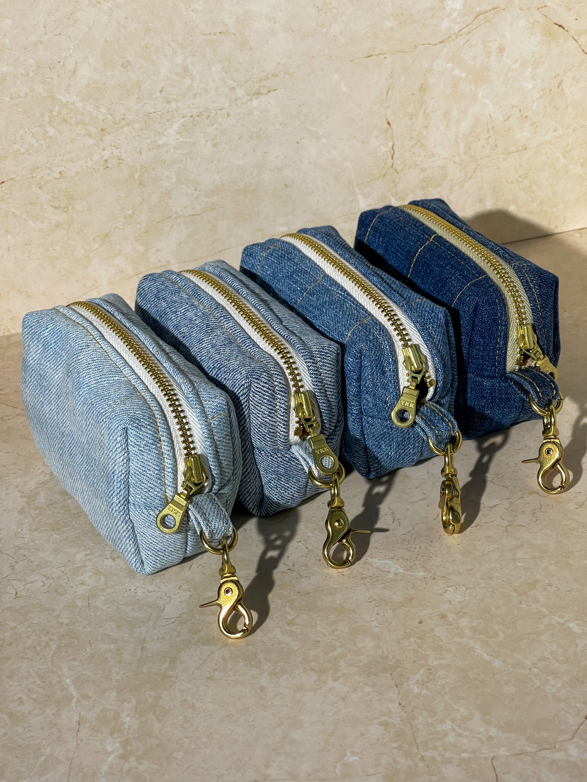Set of upcycled denim pouches with gold zippers on a beige surface
