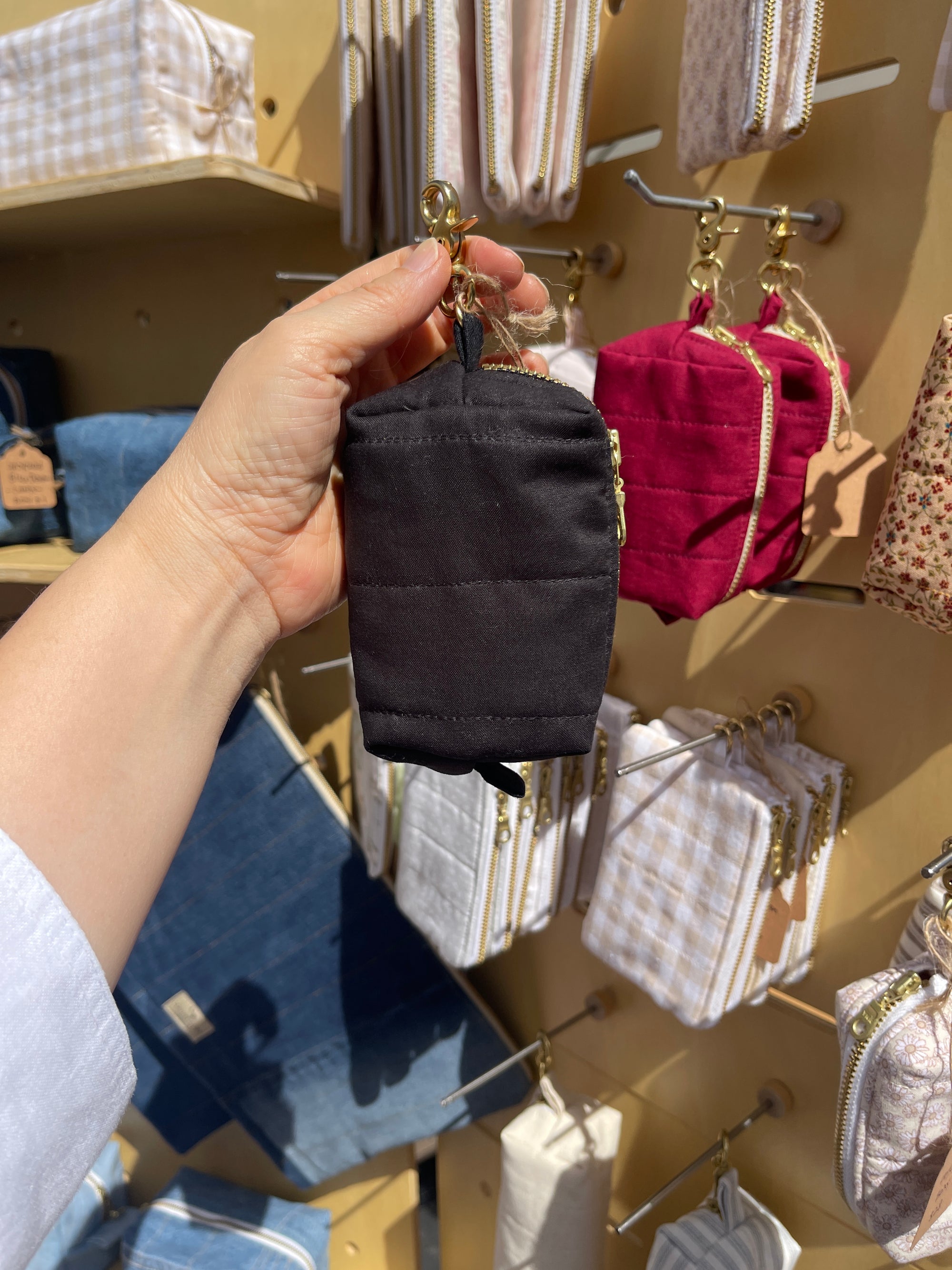 Hand holding a Lovinglog sustainable small black keychain pouch with various bags displayed in the background.