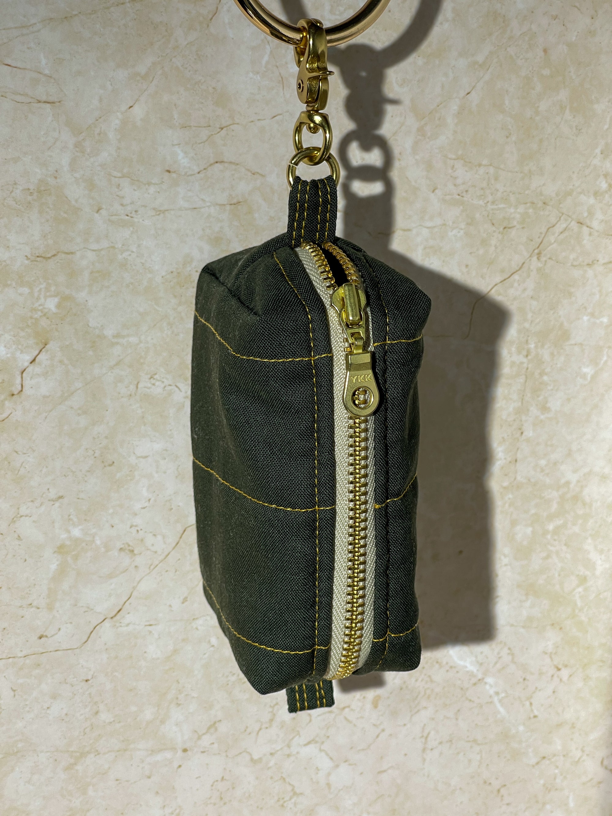 Handmade green fabric keychain pouch with gold zipper on a beige surface