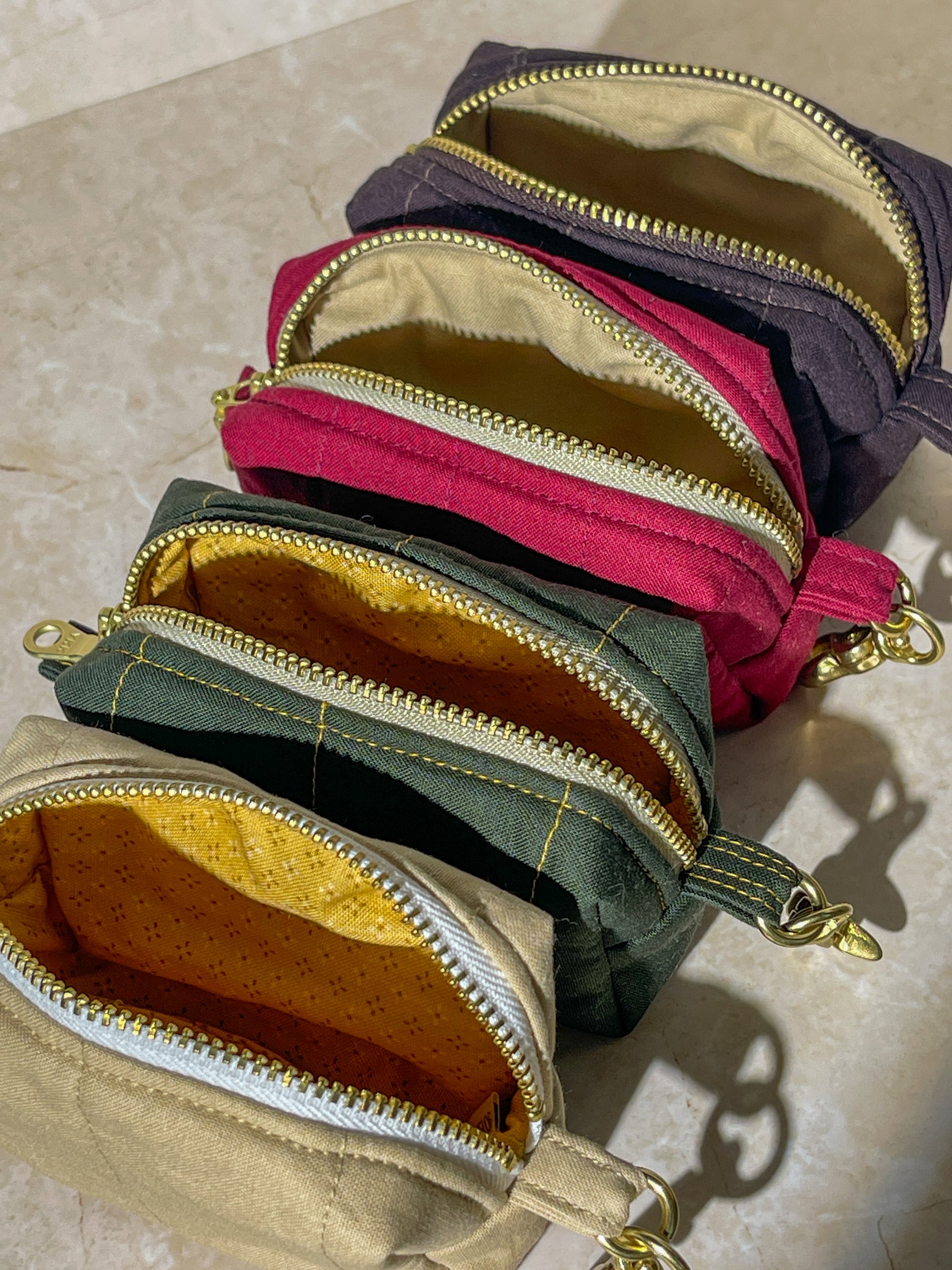 Four handmade small fabric pouches with gold zippers in different colors on a beige surface.