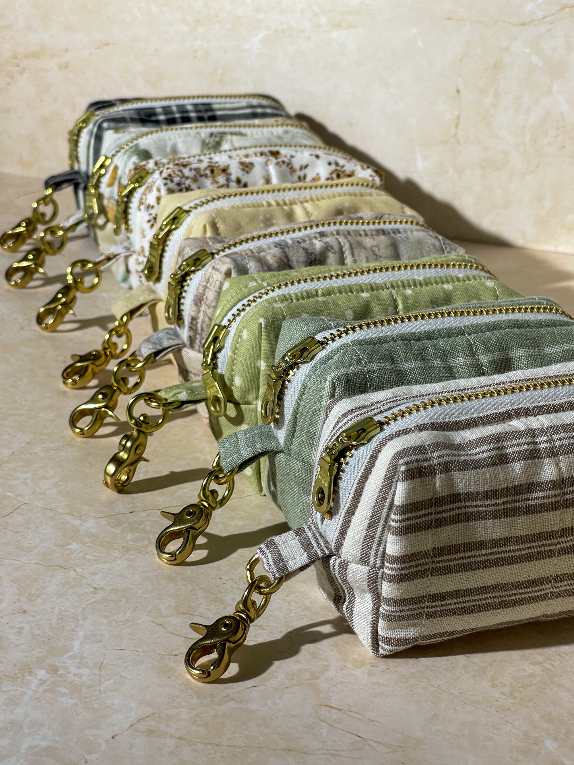 Set of small handmade fabric pouches with gold zippers on a beige surface