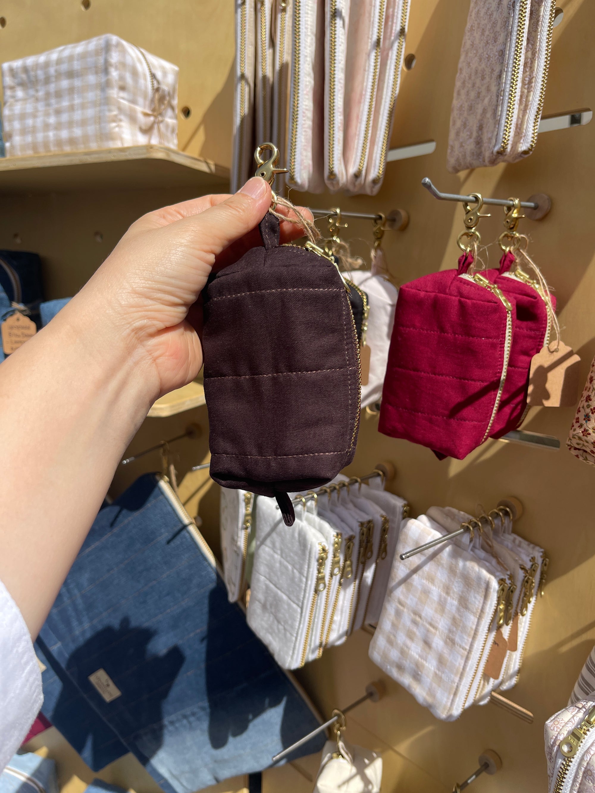 Hand holding a Lovinglog sustainable small espresso keychain pouch with various bags displayed in the background.