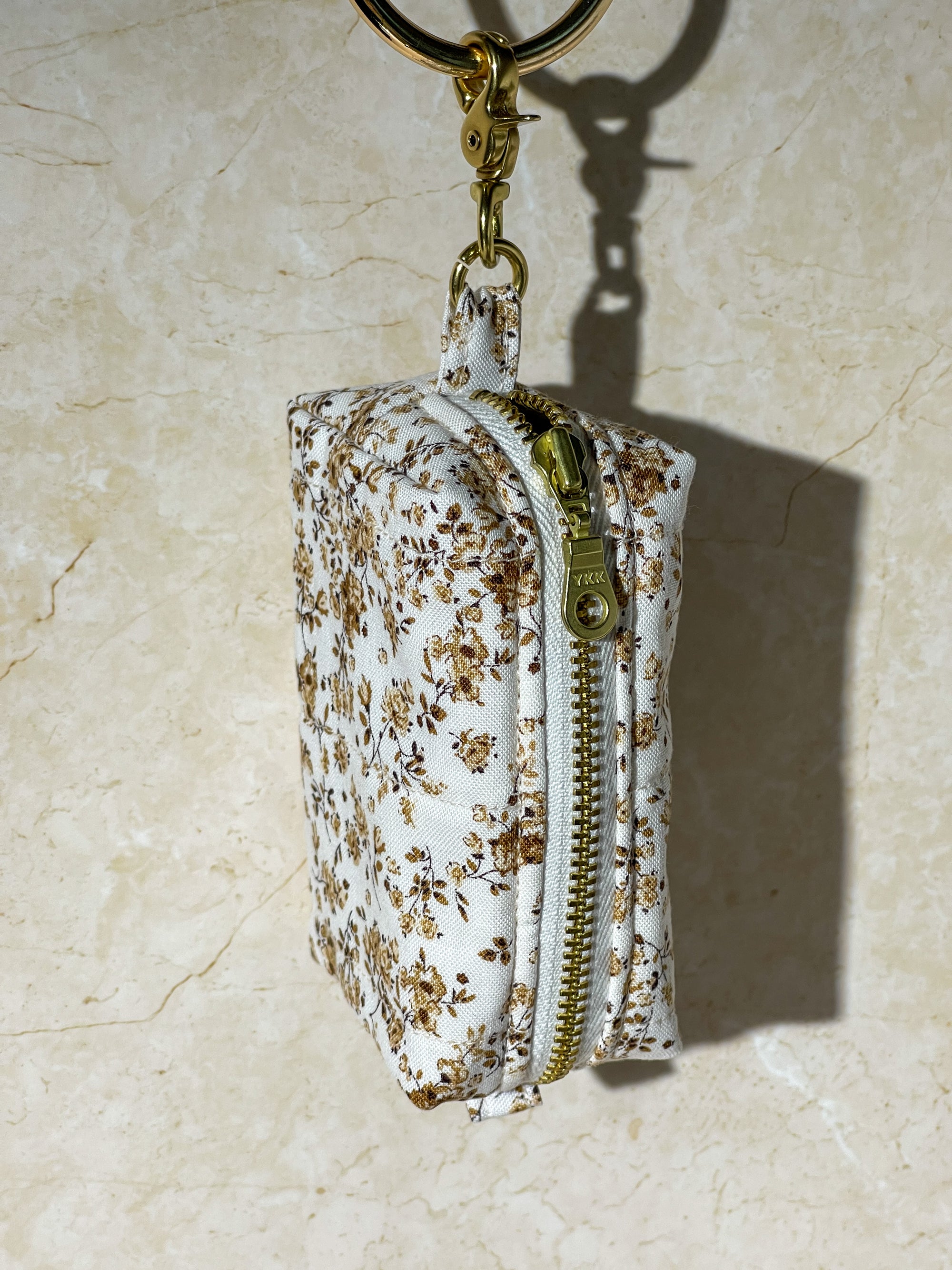 Handmade Floral-patterned pouch with a gold zipper and keychain on a beige surface