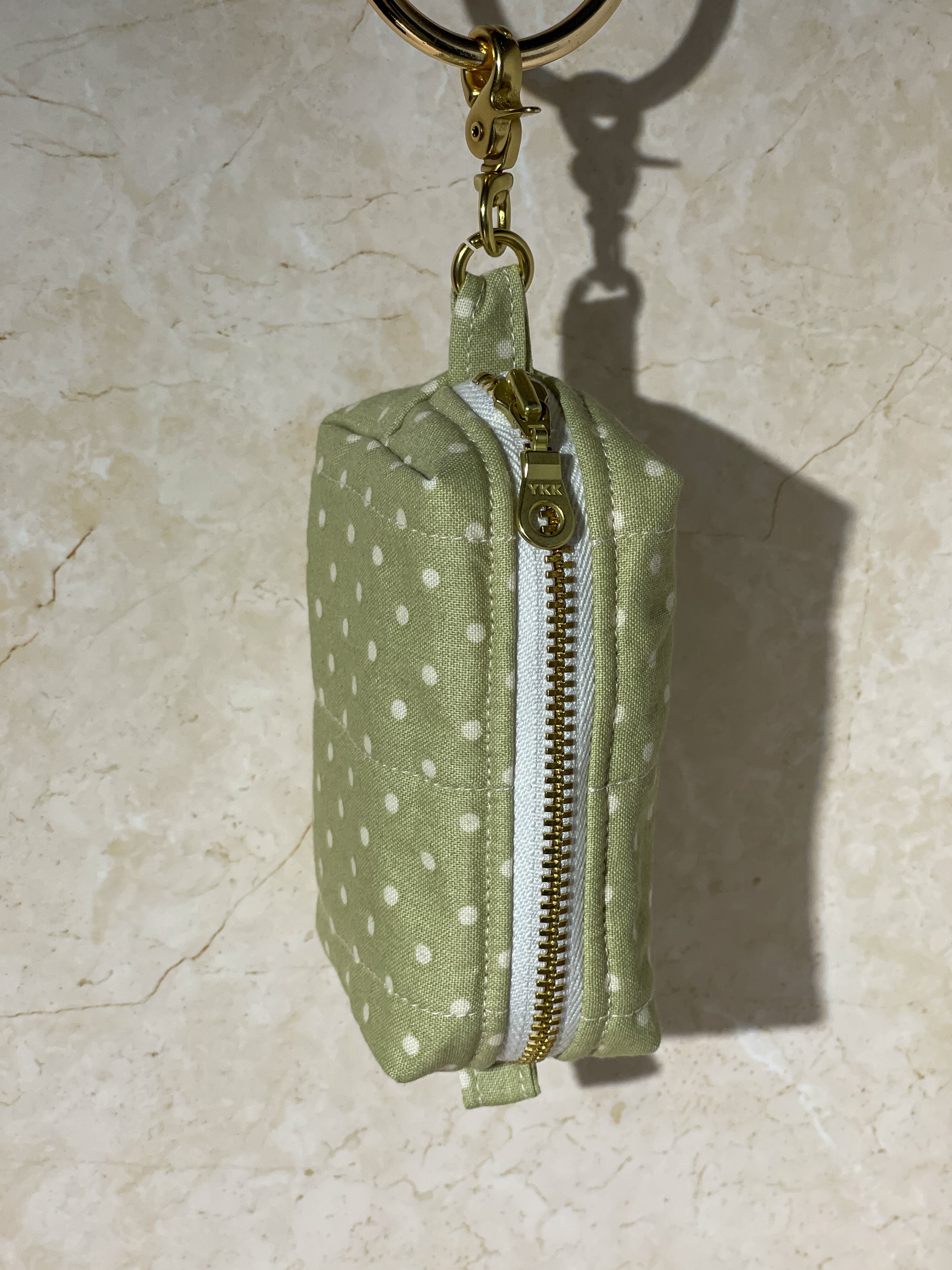 Handmade Green polka dot fabric pouch with gold zipper and keychain on a beige surface