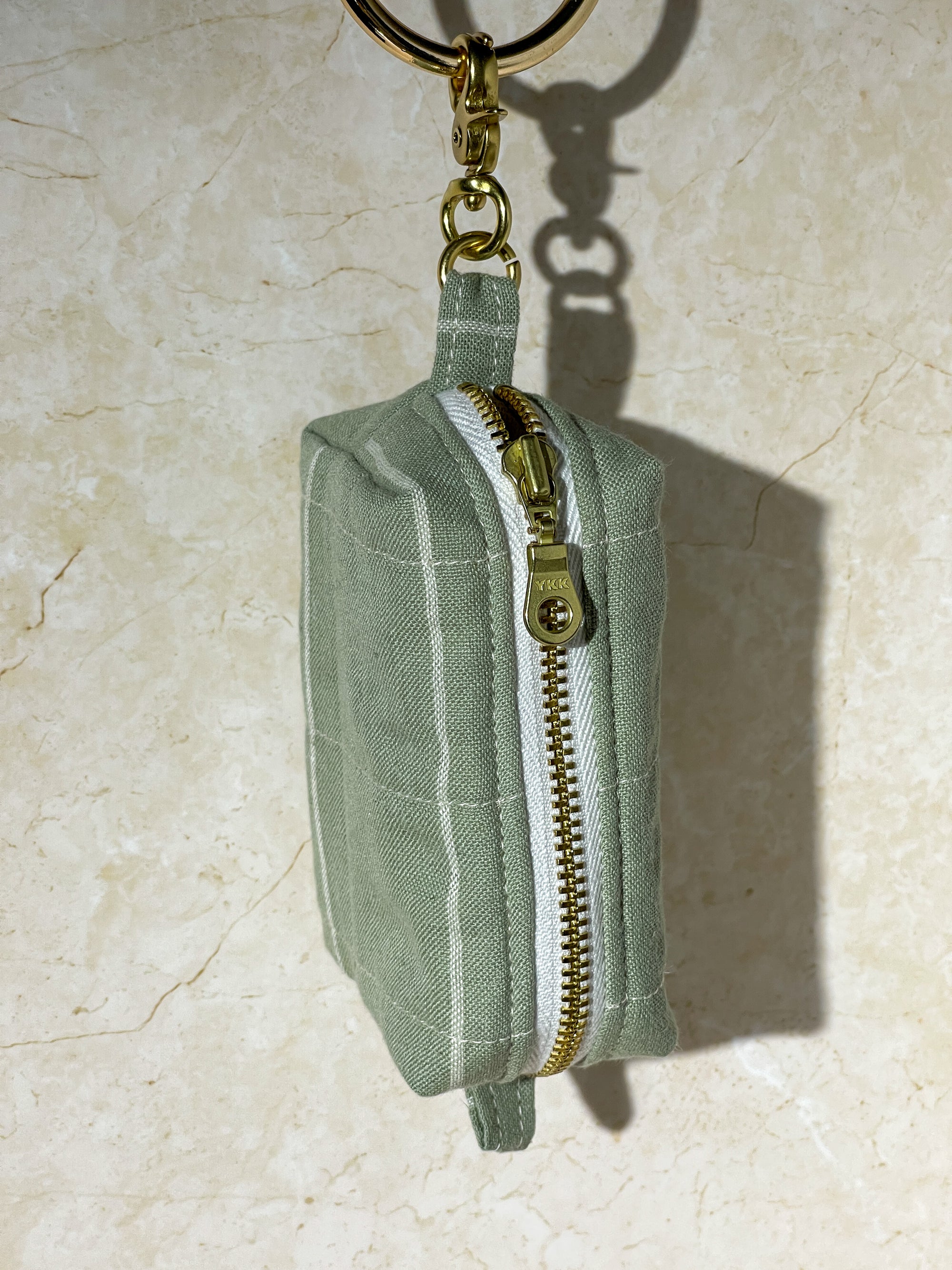 Green handmade fabric pouch with gold zipper and keychain on a beige surface