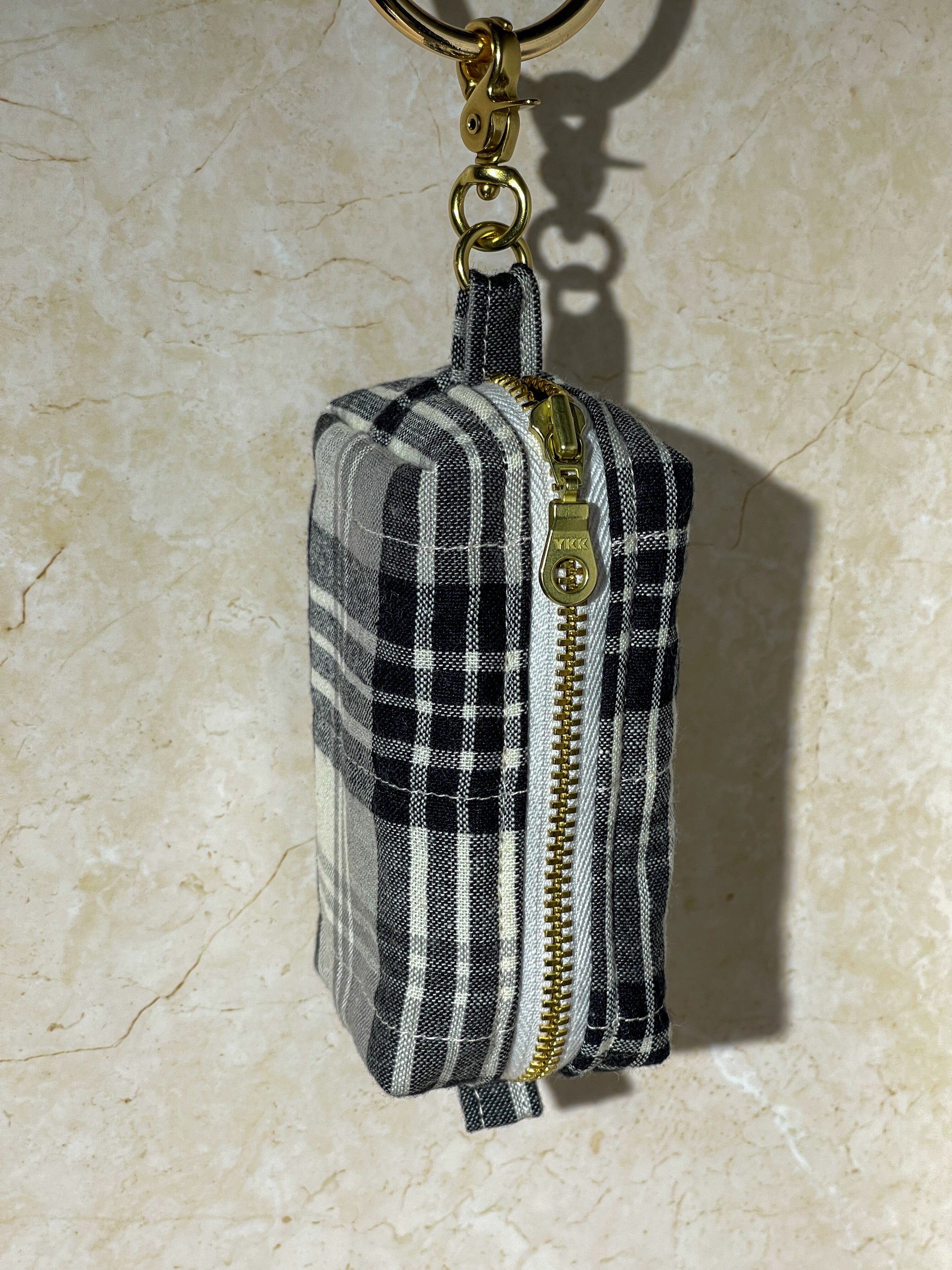 Black and white checkered handmade pouch with gold zipper and keychain on a beige surface