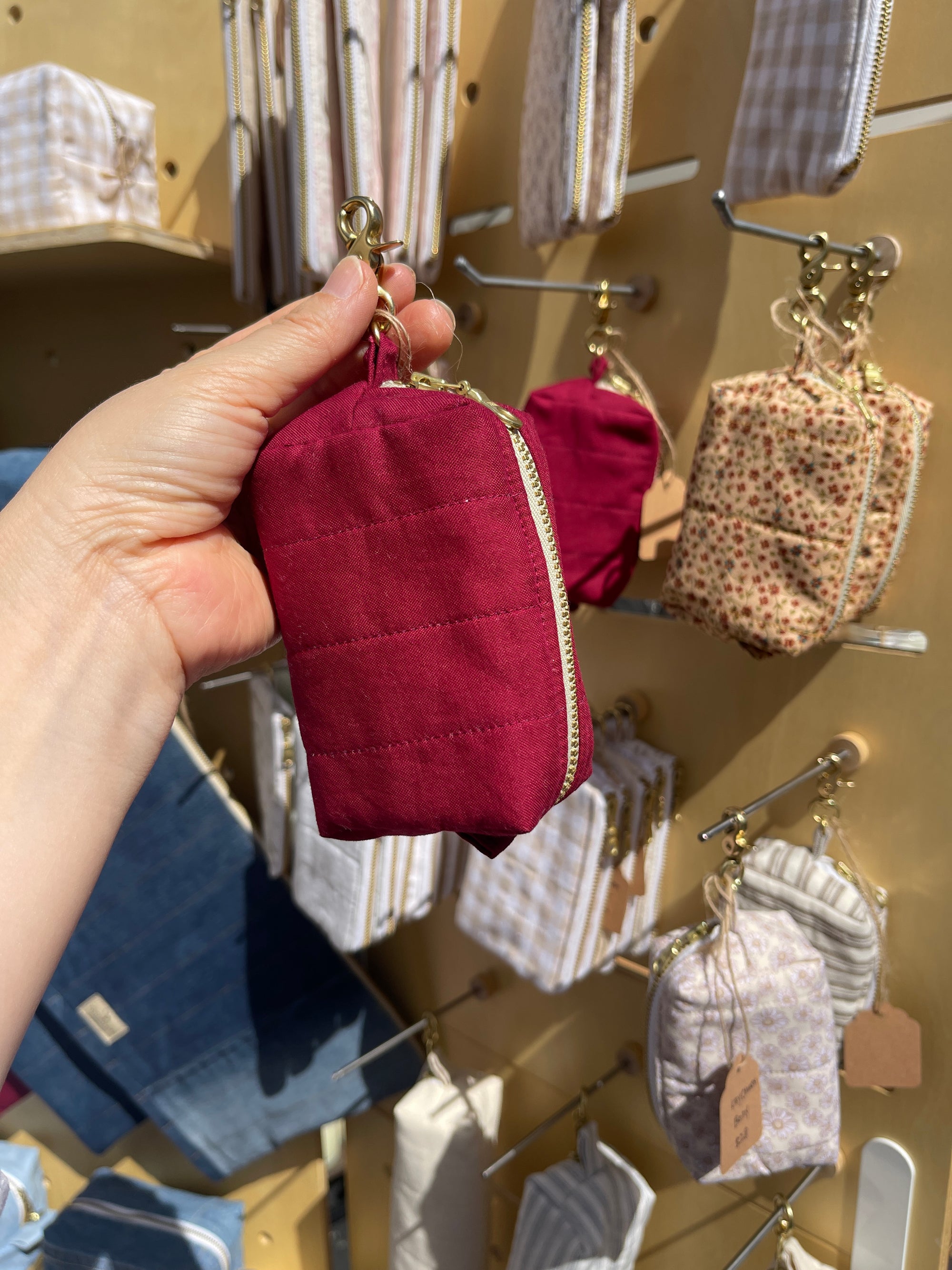 Hand holding a Lovinglog sustainable small red keychain pouch with various bags displayed in the background.