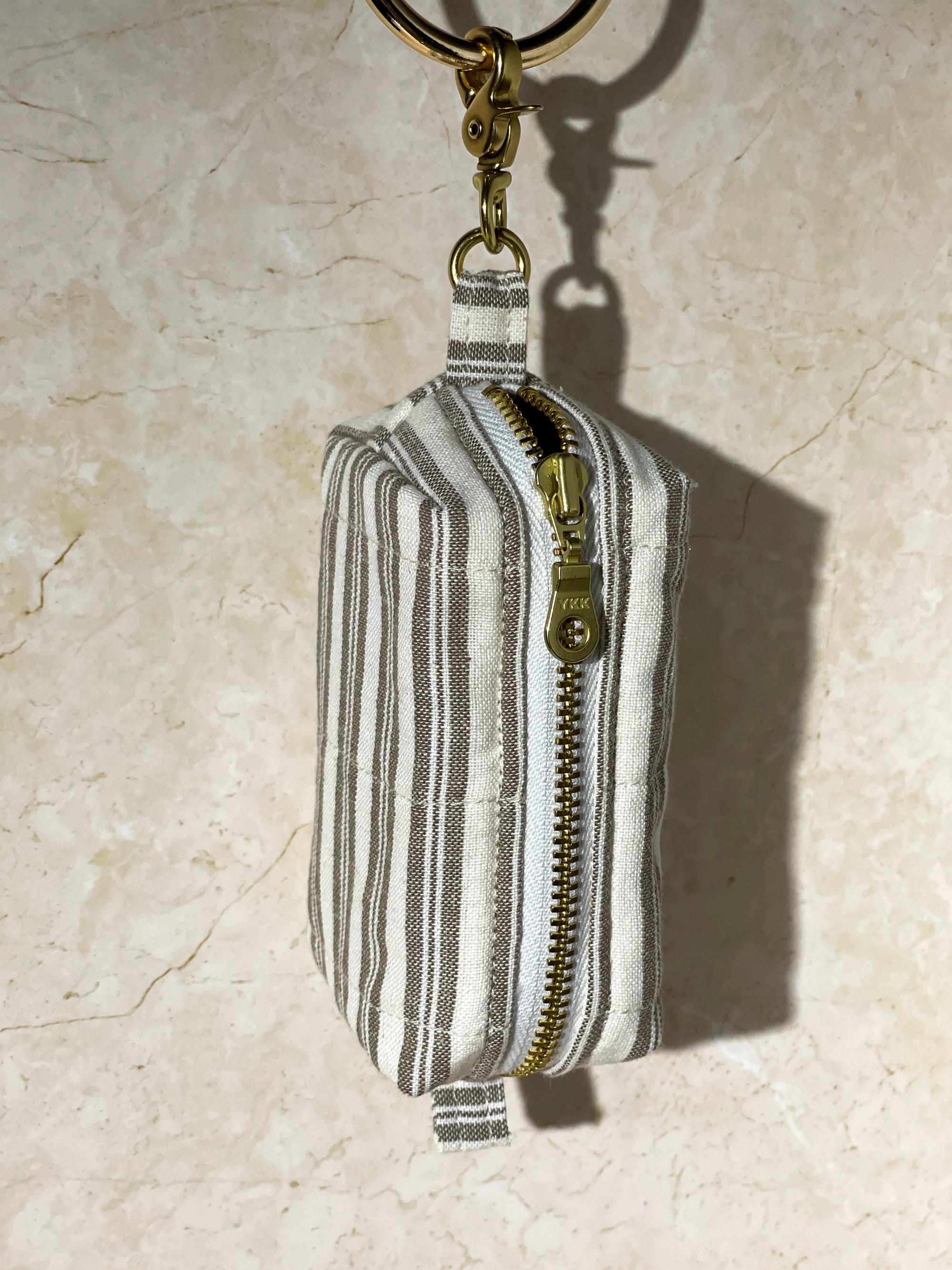 Handmade striped fabric pouch with a gold zipper and keychain on a beige background