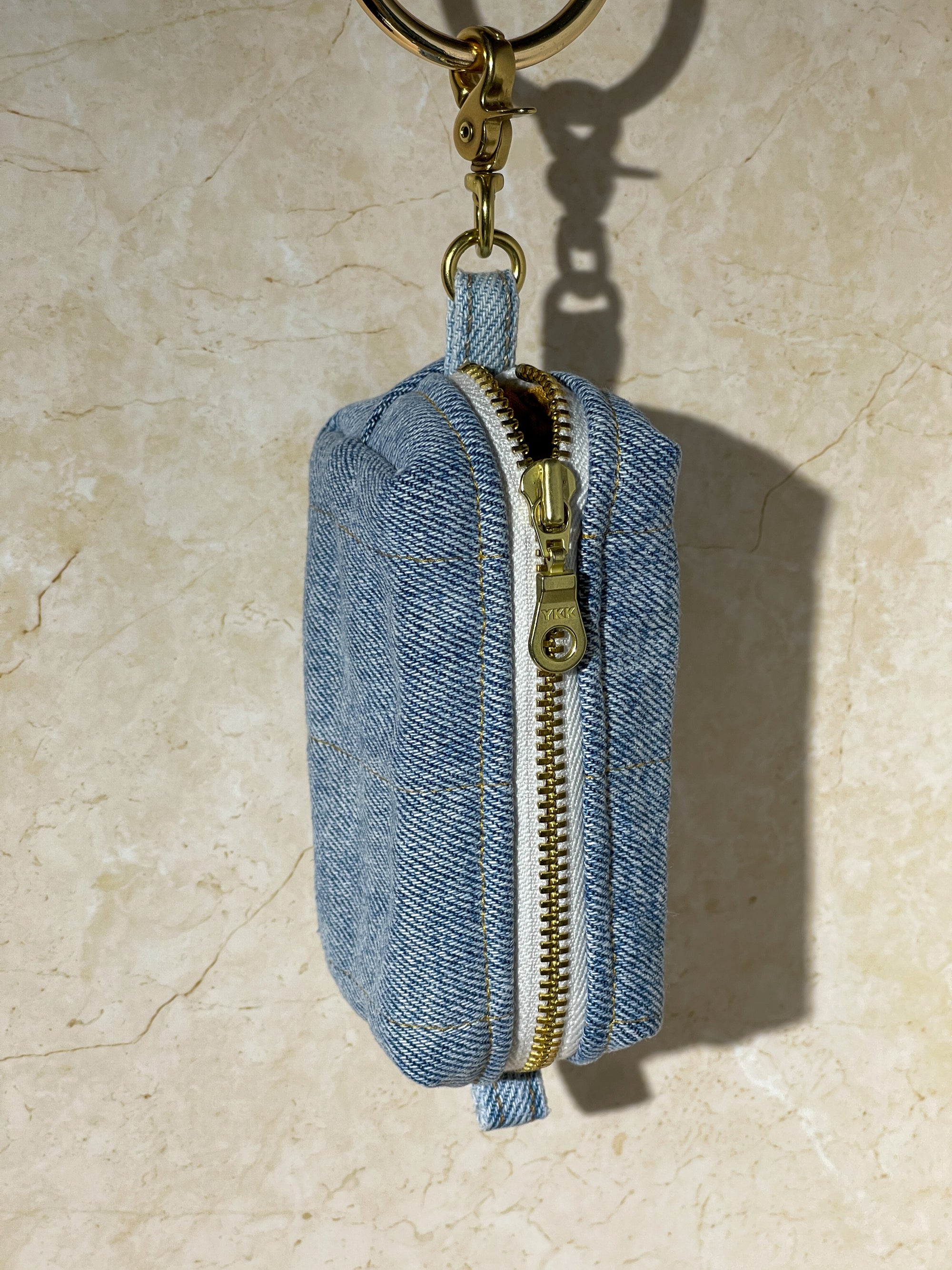 Blue handmade upcycled denim keychain pouch with gold zipper on a beige marble background