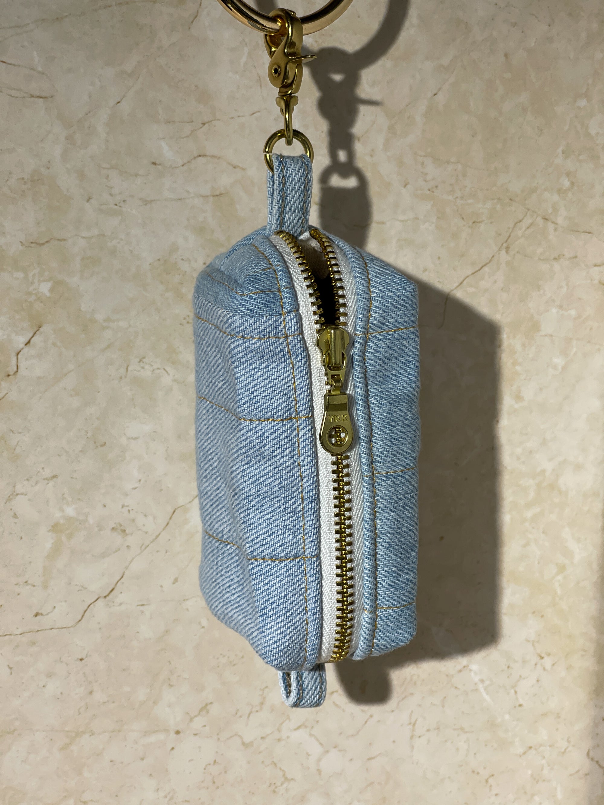 Upcycled handmade denim keychain pouch with gold zipper on a beige marble background