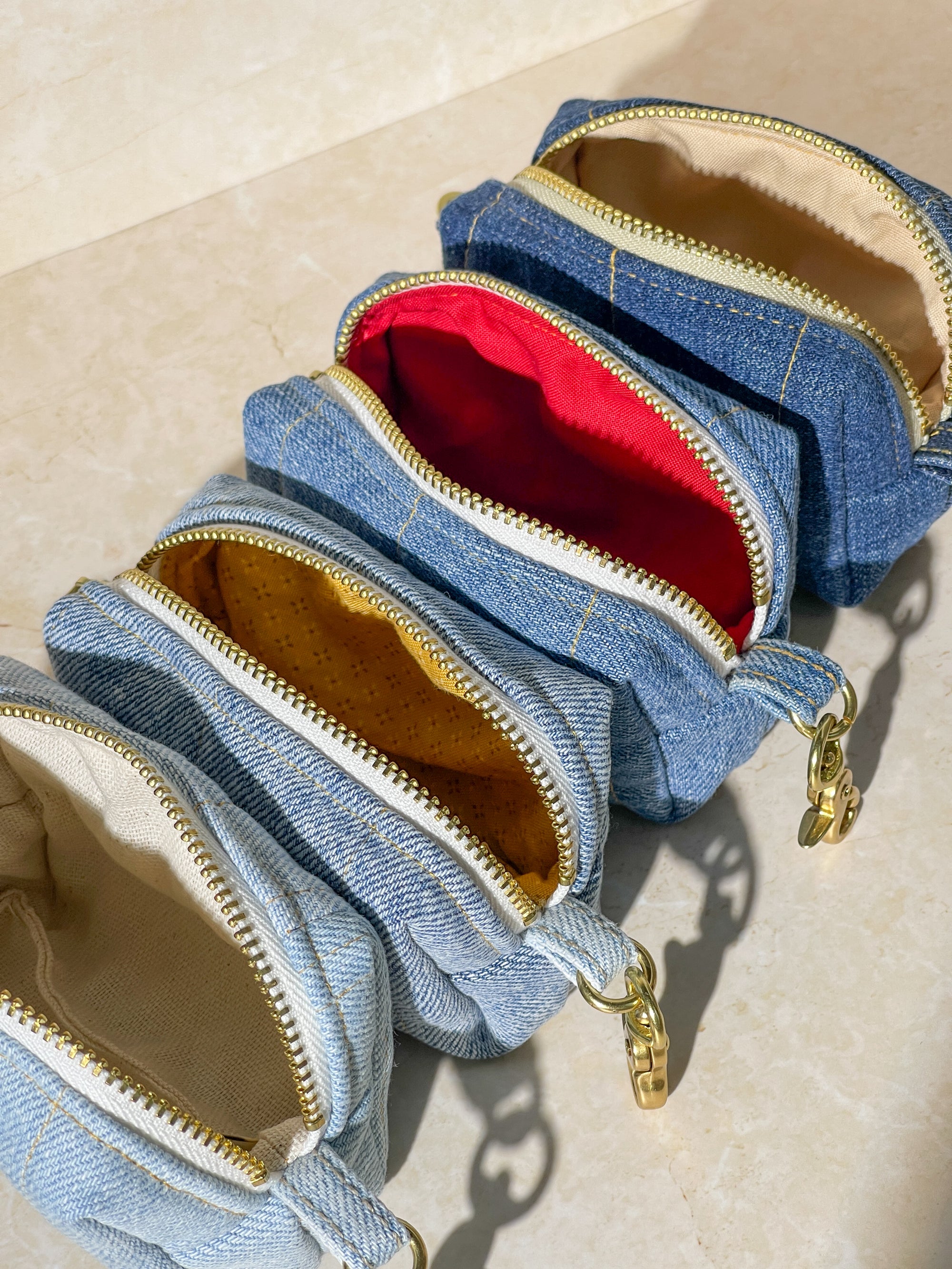 Denim upcycled pouches with gold zippers on a beige background