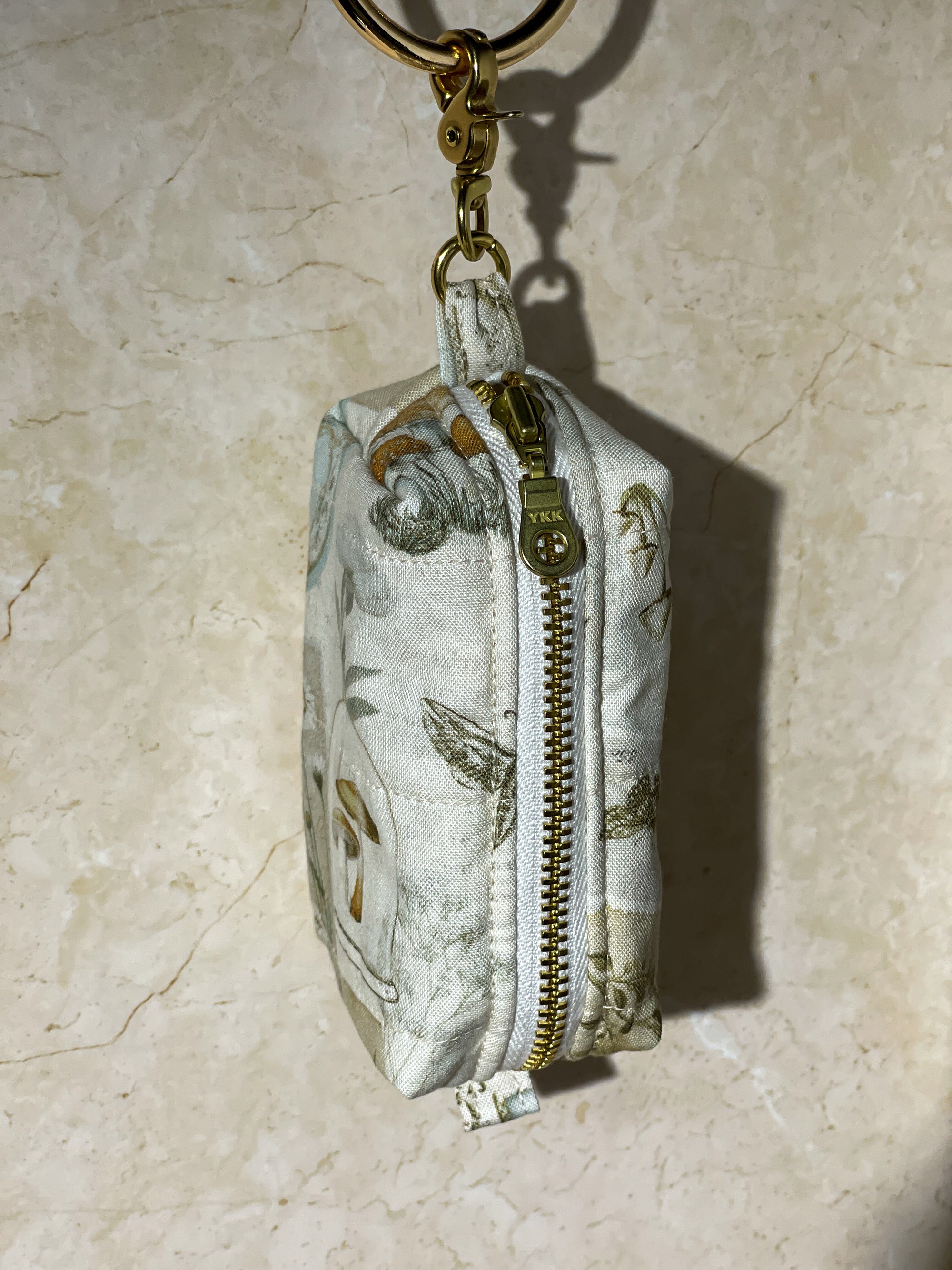Small handmade fabric pouch with a zipper and keychain attachment on a beige surface