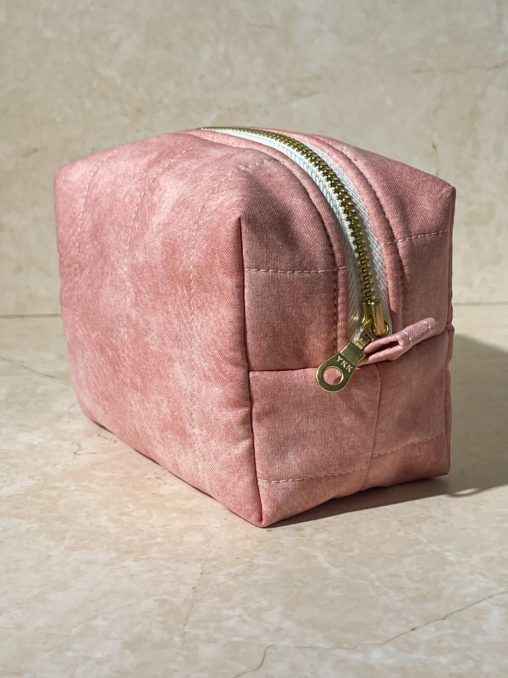 Dimensional view of the handmade sustainable quilted pink cotton boxy pouch, highlighting the gold zipper detail.