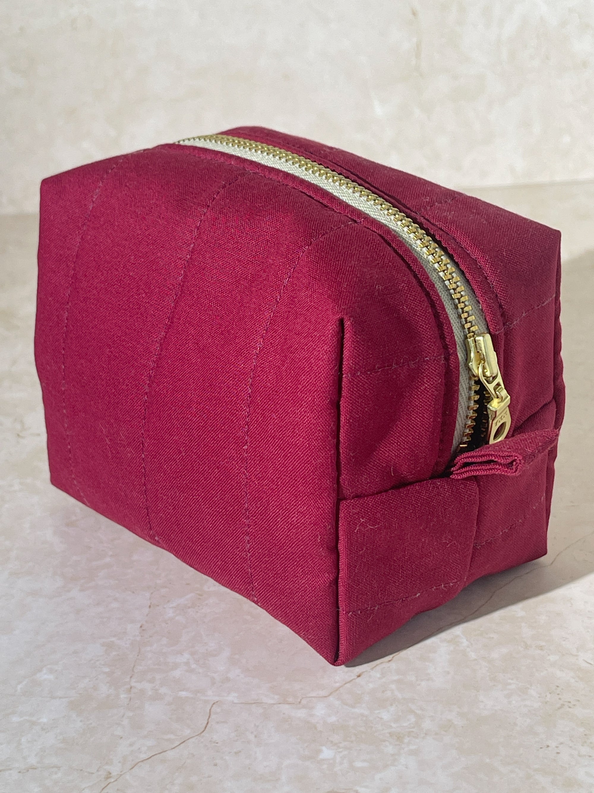 Dimensional view of the handmade sustainable quilted burgundy cotton boxy pouch, highlighting the gold zipper detail.
