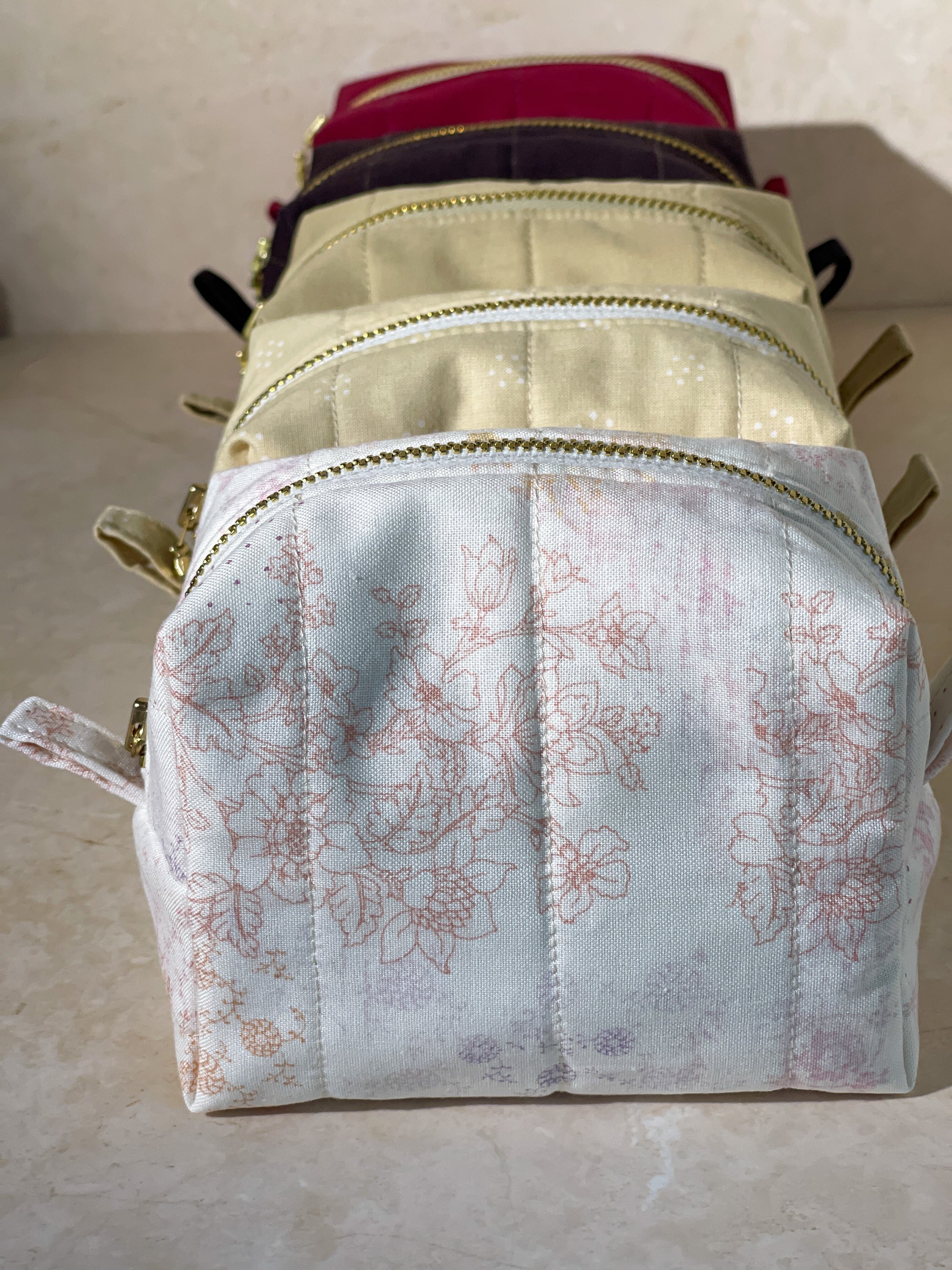 Various colors of handmade sustainable makeup pouch bags with gold zipper on a beige surface