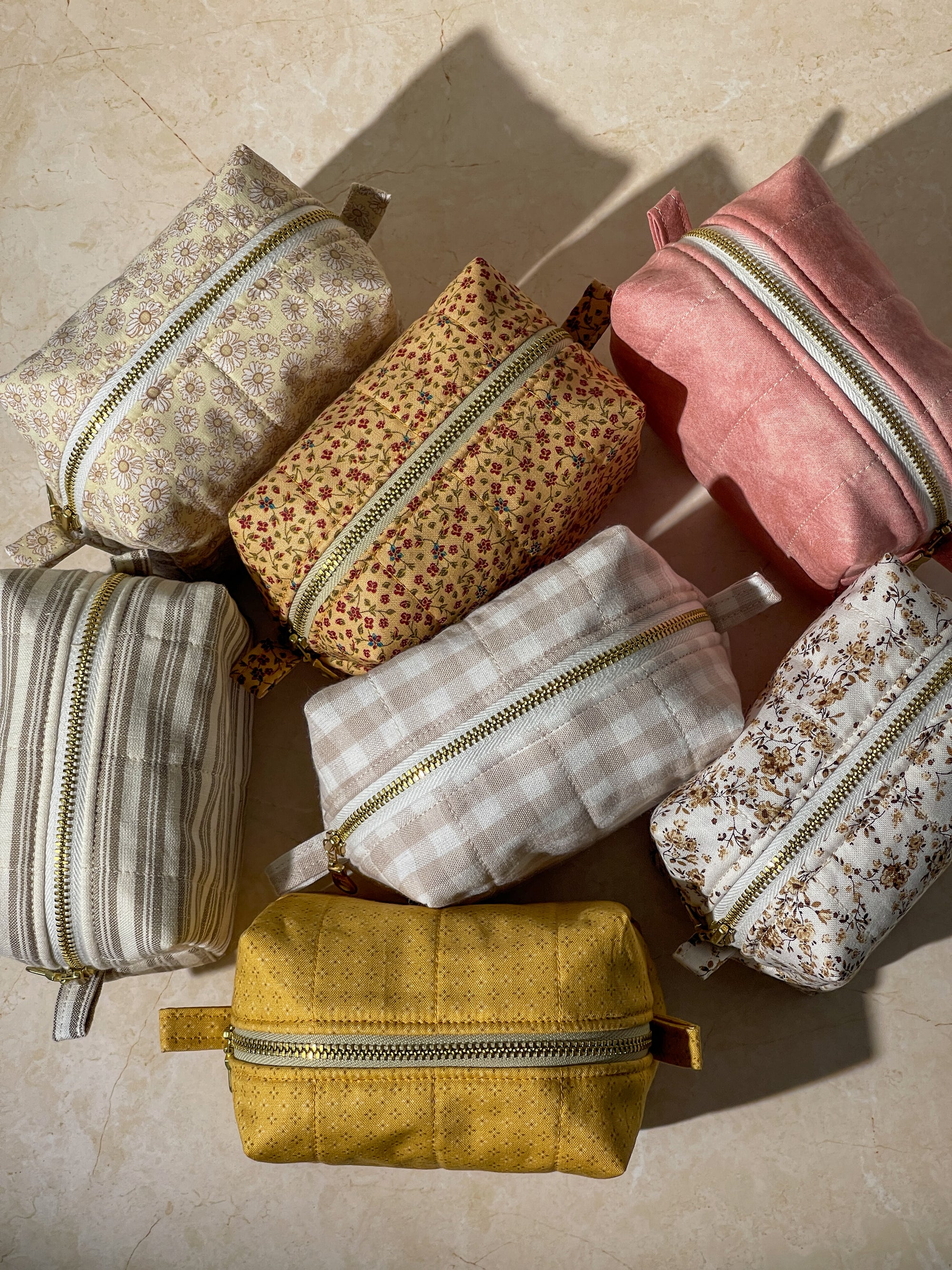 Collection of various handmade sustainable cotton makeup pouch bags with gold zippers on a beige surface