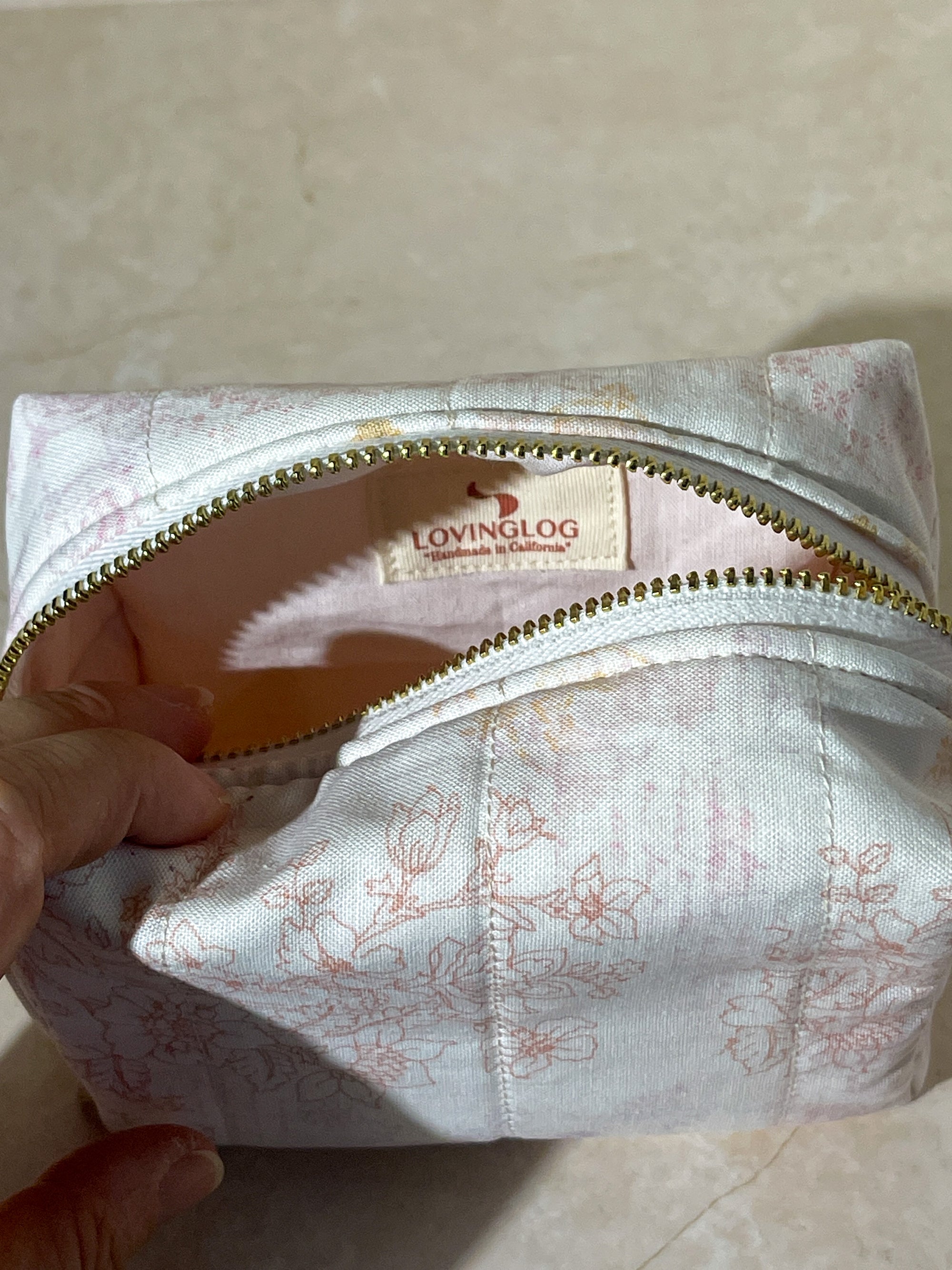 Floral-patterned handmade sustainable makeup pouch bag with gold zipper and 'LOVINGLOG' branding on a light background