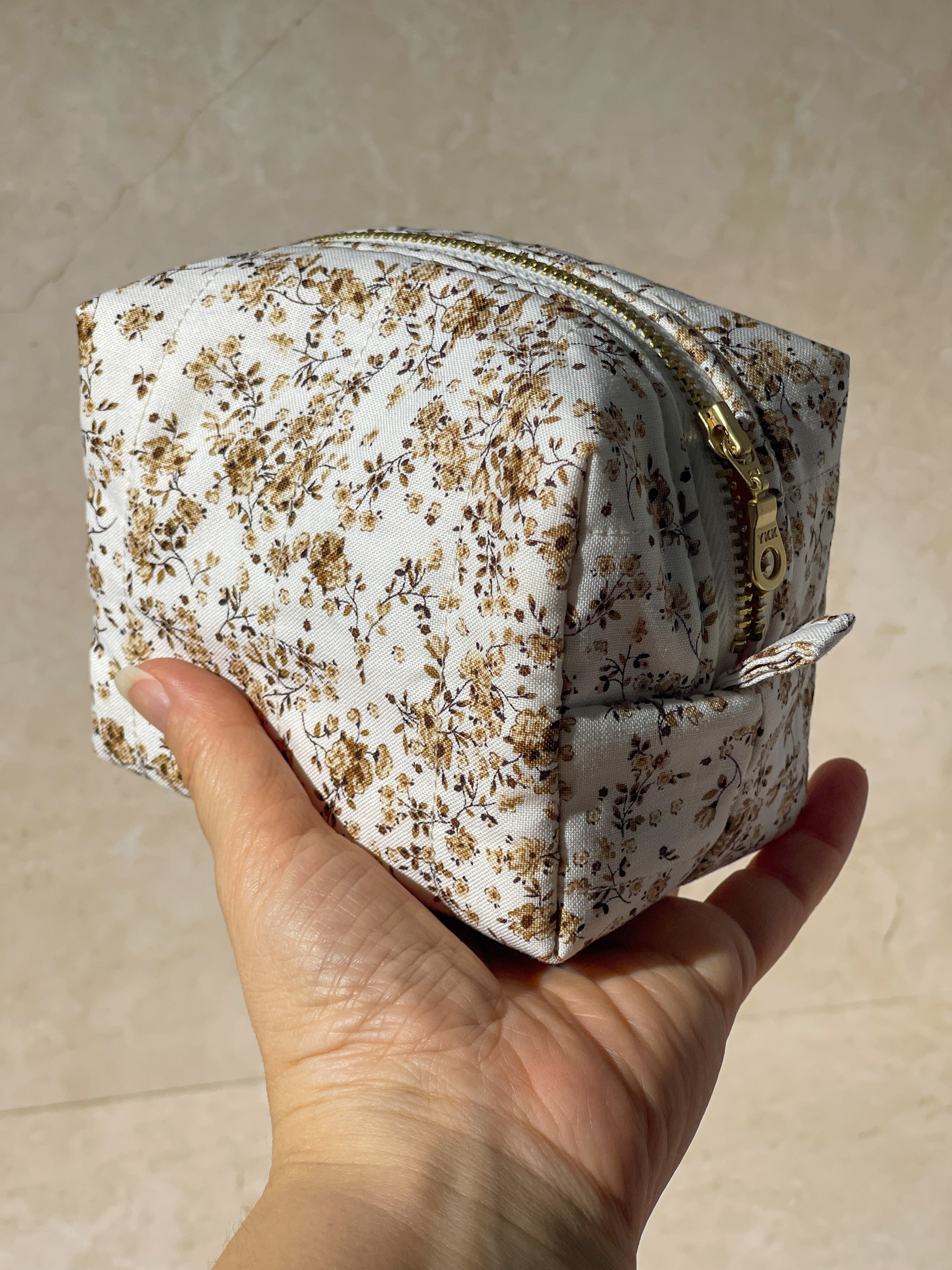 Handmade sustainable white floral-patterned makeup pouch bags held in a hand against a beige background