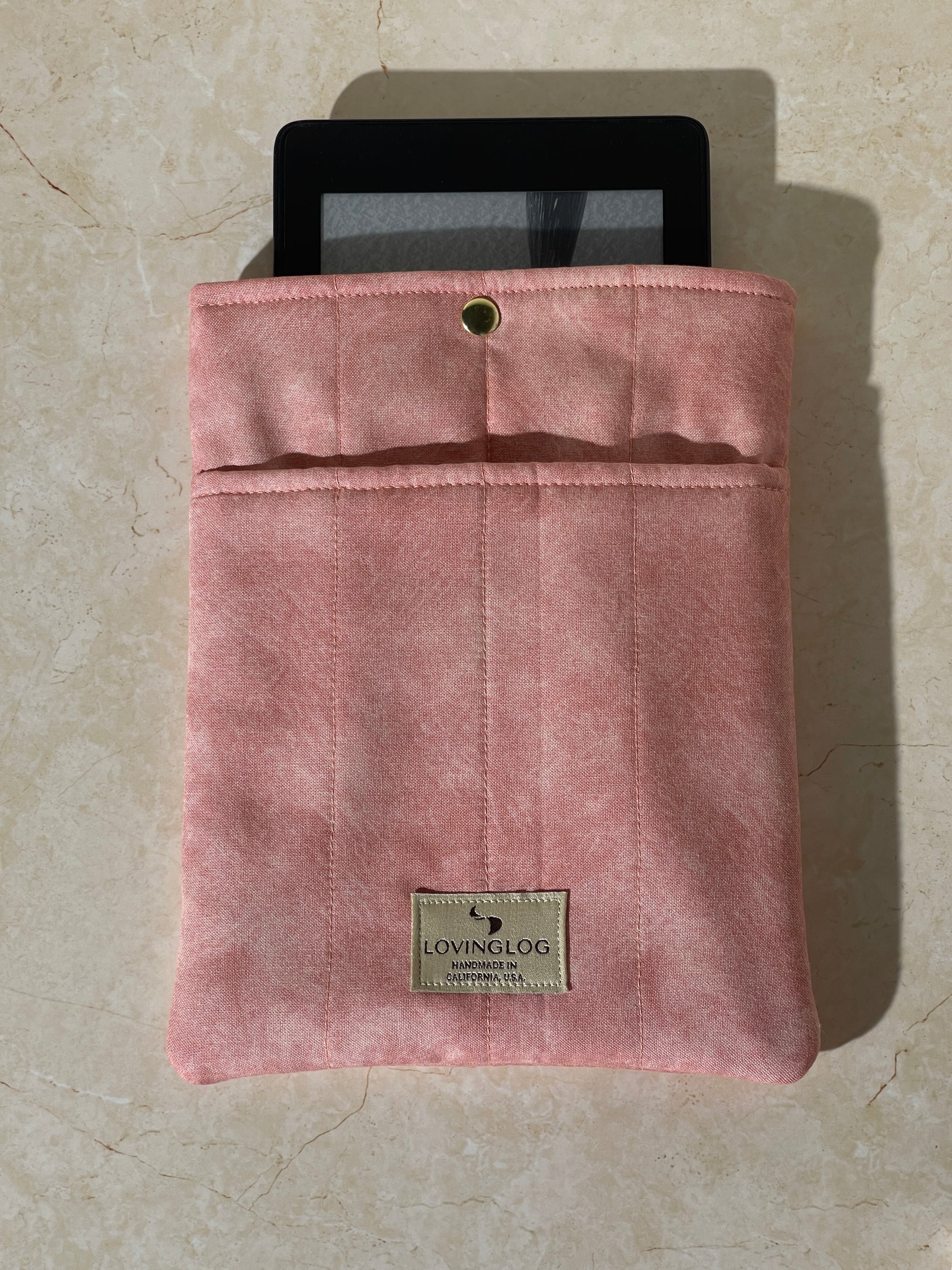 Kindle device on a Lovinglog Sustainable pink cotton books, kindle sleeve on a beige surface