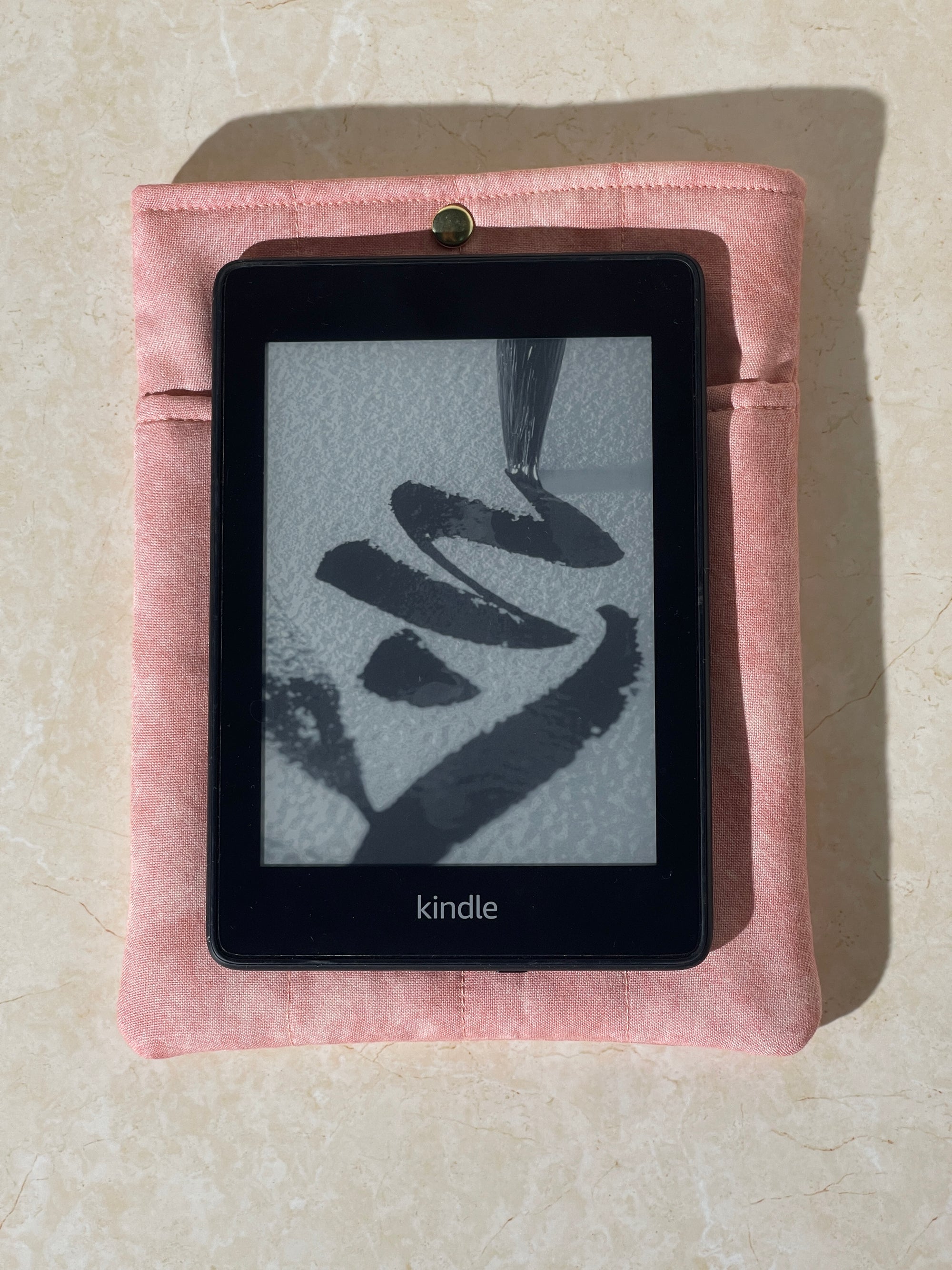 Kindle device on a Lovinglog Sustainable pink cotton books, kindle sleeve on a beige surface