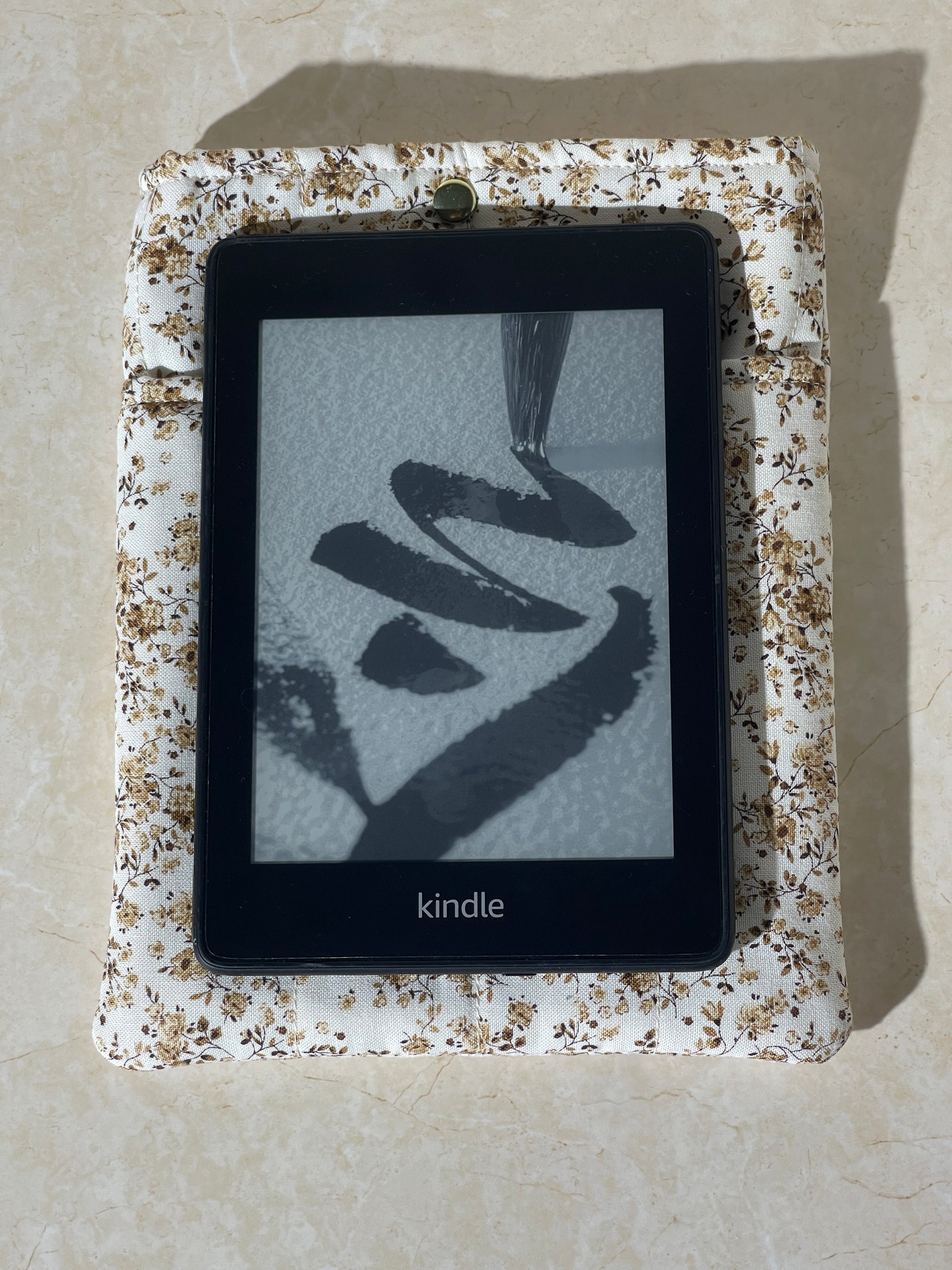 Kindle device on a Lovinglog Sustainable white floral pattern cotton books, kindle sleeve on a beige surface